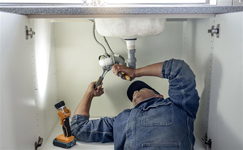 Plumber repairing pipes beneath a bathroom sink in Canton