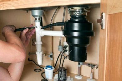 Plumber repairing a garbage disposal beneath a kitchen sink in Canton