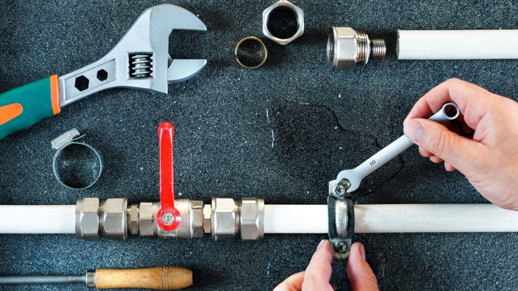 Plumber repairing a pipe valve with an adjustable wrench in Canton