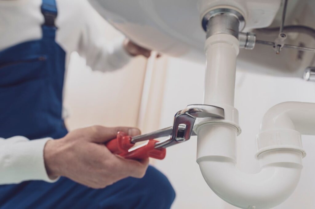 Plumber repairing a white drain pipe beneath a sink in Canton