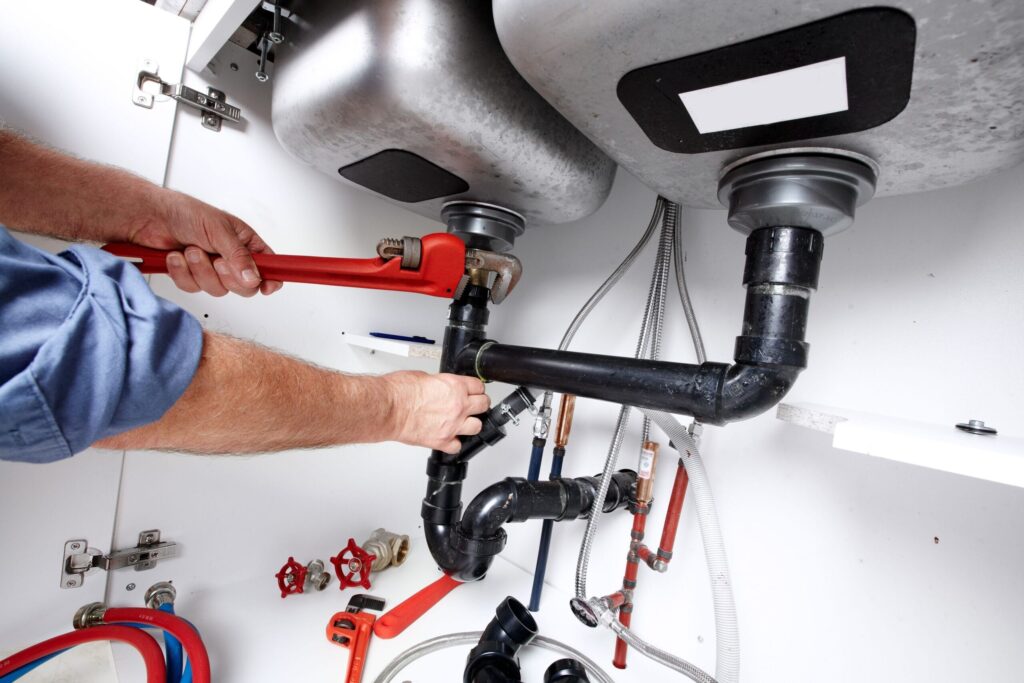 Plumber repairing drain pipes beneath a kitchen sink in Canton