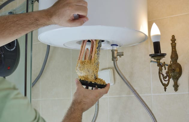 Technician removing mineral buildup from a water heater in Canton